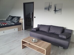 A modern living room with a sofa, a coffee table, and a bed with a cityscape bedspread. - Alpine view (Sigmarszell)