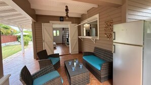 A covered patio area with wicker furniture, a refrigerator, and a hanging light fixture. - Villa rose des sables with private pool (Saint-François)