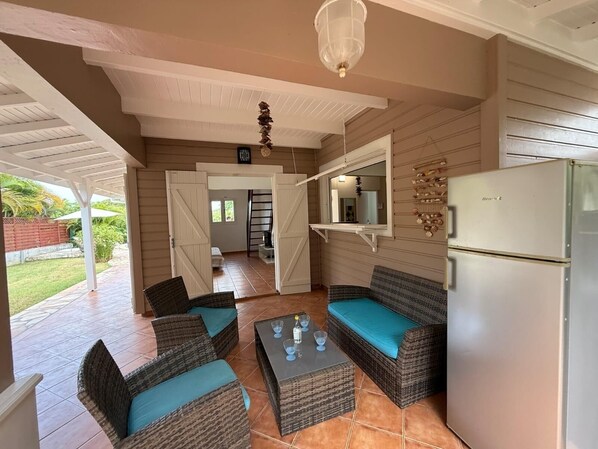 A covered patio area with wicker furniture, a refrigerator, and a hanging light fixture.