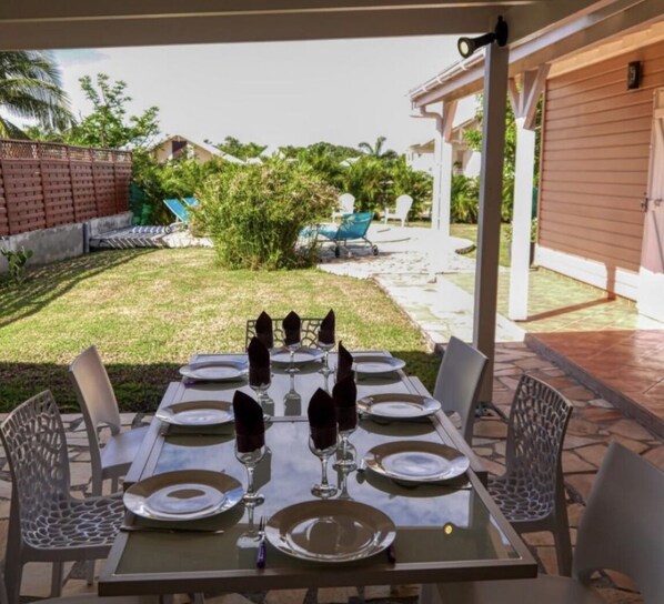 A covered outdoor dining area with a table set for six, surrounded by chairs.