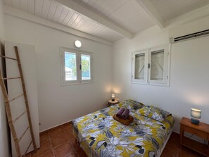 A bedroom with a bed, two windows, a ladder, a nightstand with a lamp, and a wall-mounted air conditioner.