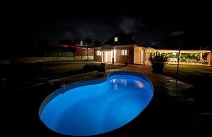 A swimming pool at night with a house in the background.