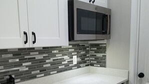 Una cocina con armarios blancos, un microondas negro, salpicadero de azulejos y un grifo negro.