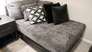 Un sofá gris con estructura negra, acompañado por una mesita de noche y una lámpara.