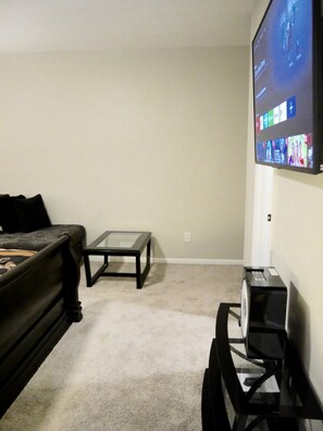 A living room with a couch, a coffee table, a TV mounted on the wall, and a small black speaker.