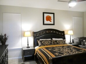 A bedroom with a large bed, two bedside tables with lamps, a ceiling fan, and a framed picture on the wall.