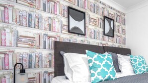 A bedroom with a bookshelf wall, a grey headboard, and patterned pillows. - Three Bedroom Apartment by Klass Living Serviced Accommodation Coatbridge - Berwick Apartment With WiFi &Parking (Coatbridge)