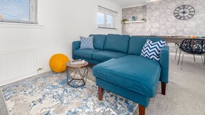 A modern living room with a blue sectional sofa, a small round table, and a patterned rug. - Three Bedroom Apartment by Klass Living Serviced Accommodation Coatbridge - Berwick Apartment With WiFi &Parking (Coatbridge)