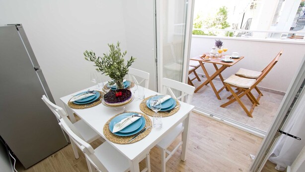 A dining area with a white table set for two, a potted plant, and a view of the balcony. - Cozy, modern,new apartments - 1 minute from the beach (Drašnice)