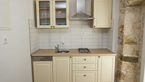 A compact kitchen with white cabinets, a gas stove, a dishwasher, and a stone wall. - Cozy, modern,new apartments - 1 minute from the beach (Drašnice)