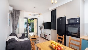 En moderne stue med sofa, spisebord og tekøkken med køleskab og mikrobølgeovn.