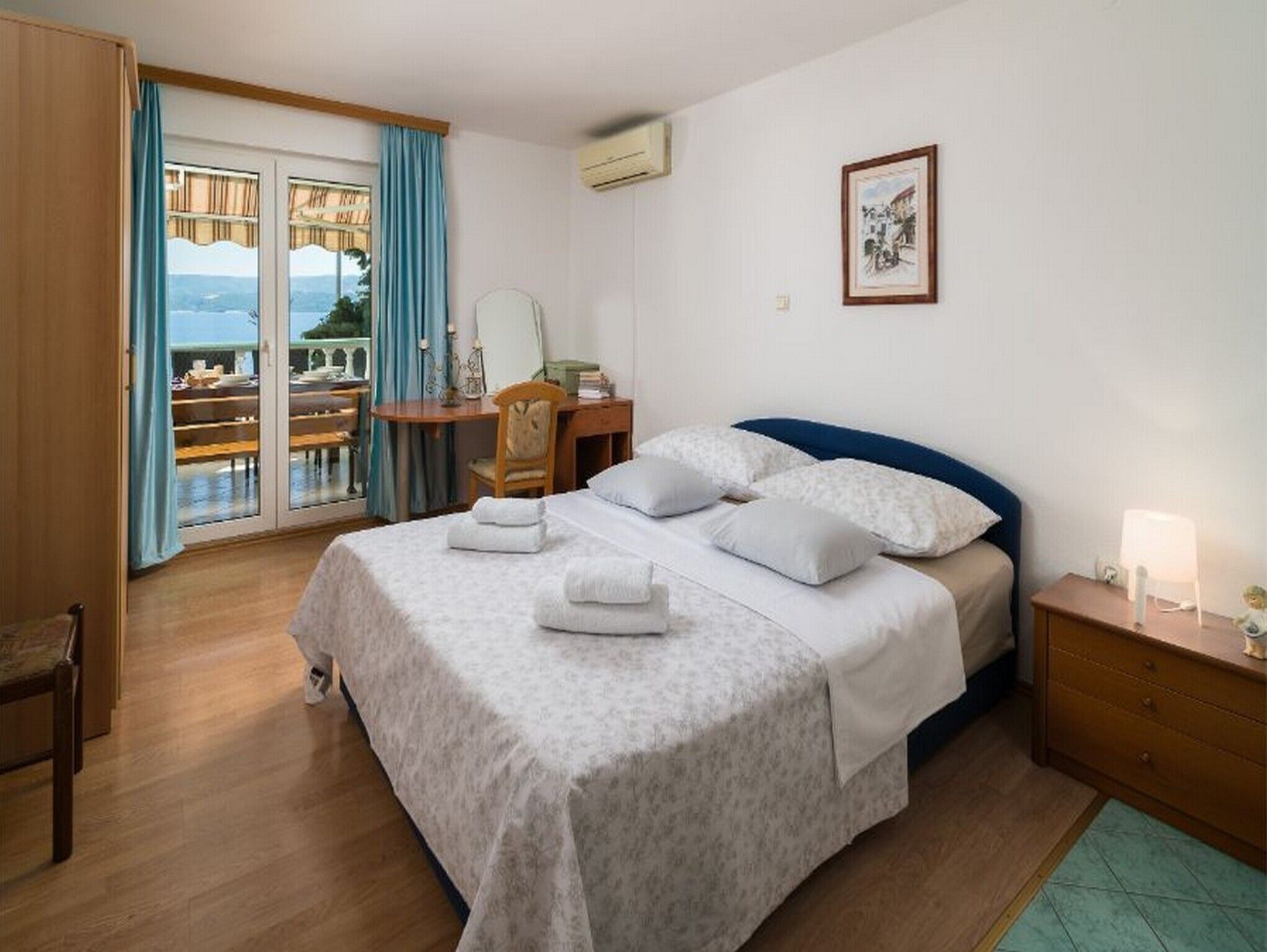 Ein Schlafzimmer mit Bett, Schreibtisch, Stuhl, Nachttisch und Blick durch eine Schiebetür.