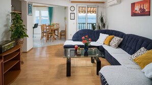 Ein Wohnzimmer mit einem dunkelblauen Sofa, einem Glastisch und einem Essbereich mit Holzsesseln und einem Tisch.