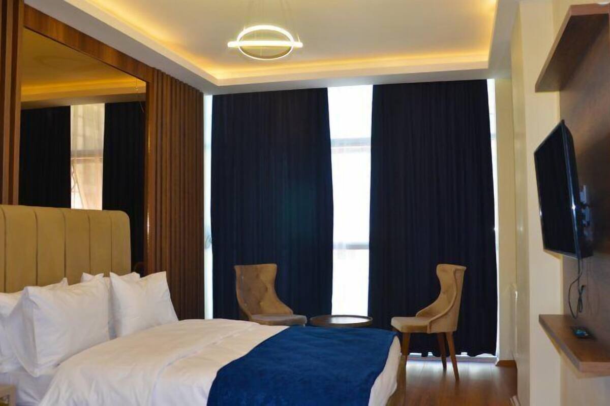 Habitación de hotel con una cama grande, dos sillas, un televisor y un ventanal con cortinas.