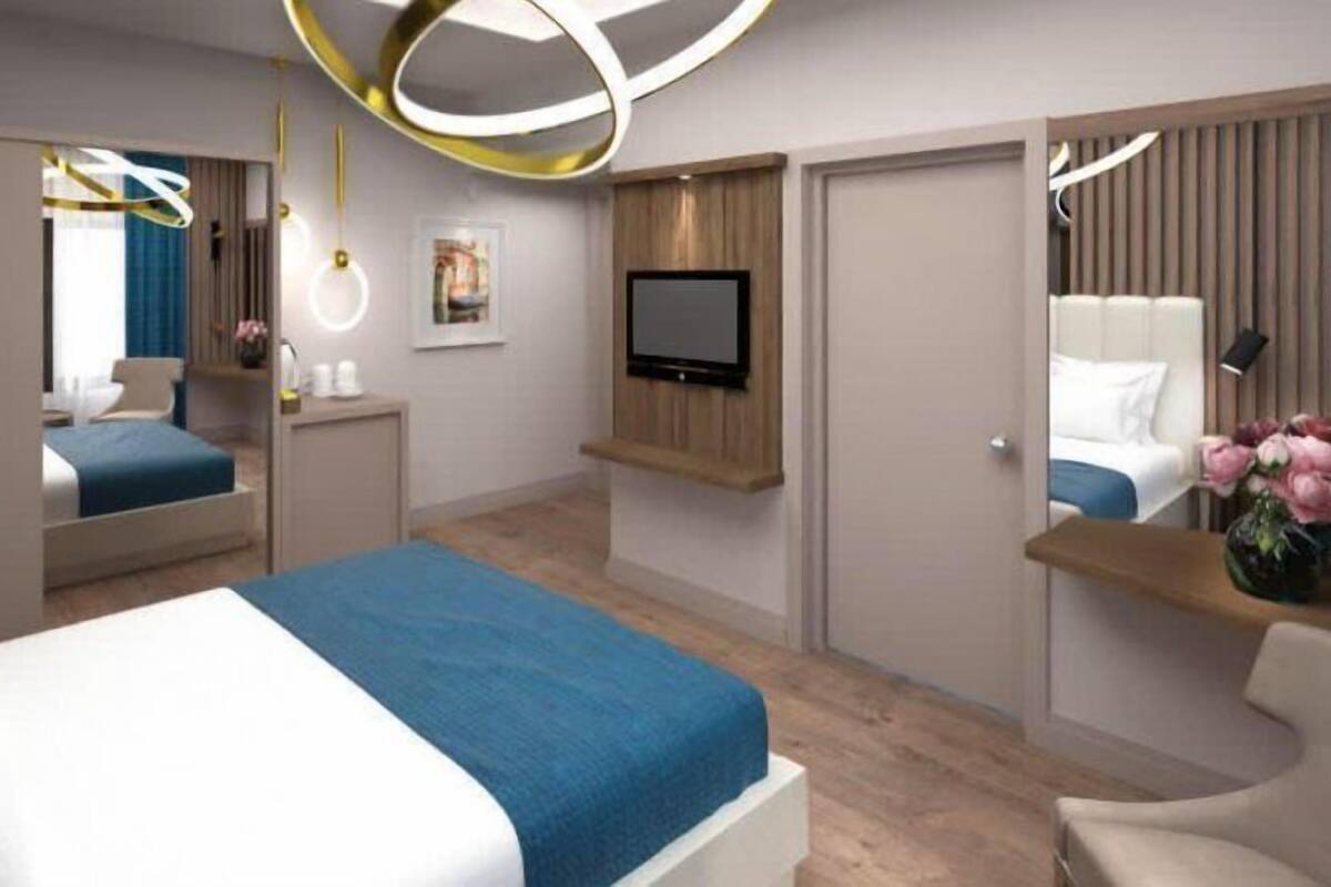 Una habitación de hotel moderna con una cama grande, un televisor montado en la pared, un escritorio con una silla y un espejo.