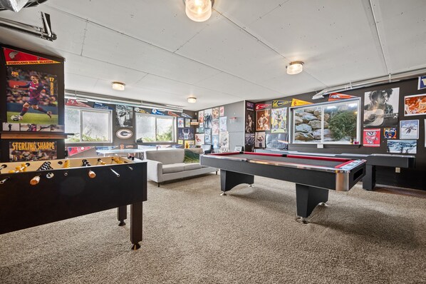 A room with a foosball table, pool table, and various sports memorabilia on the walls.