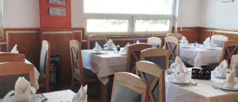 A restaurant with multiple tables set for dining, each with white tablecloths and neatly arranged napkins.