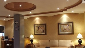 A well-lit lobby with a sofa, two lamps, a coffee table, and two framed artworks on the wall. - Hotel La Muralla (Toluca)