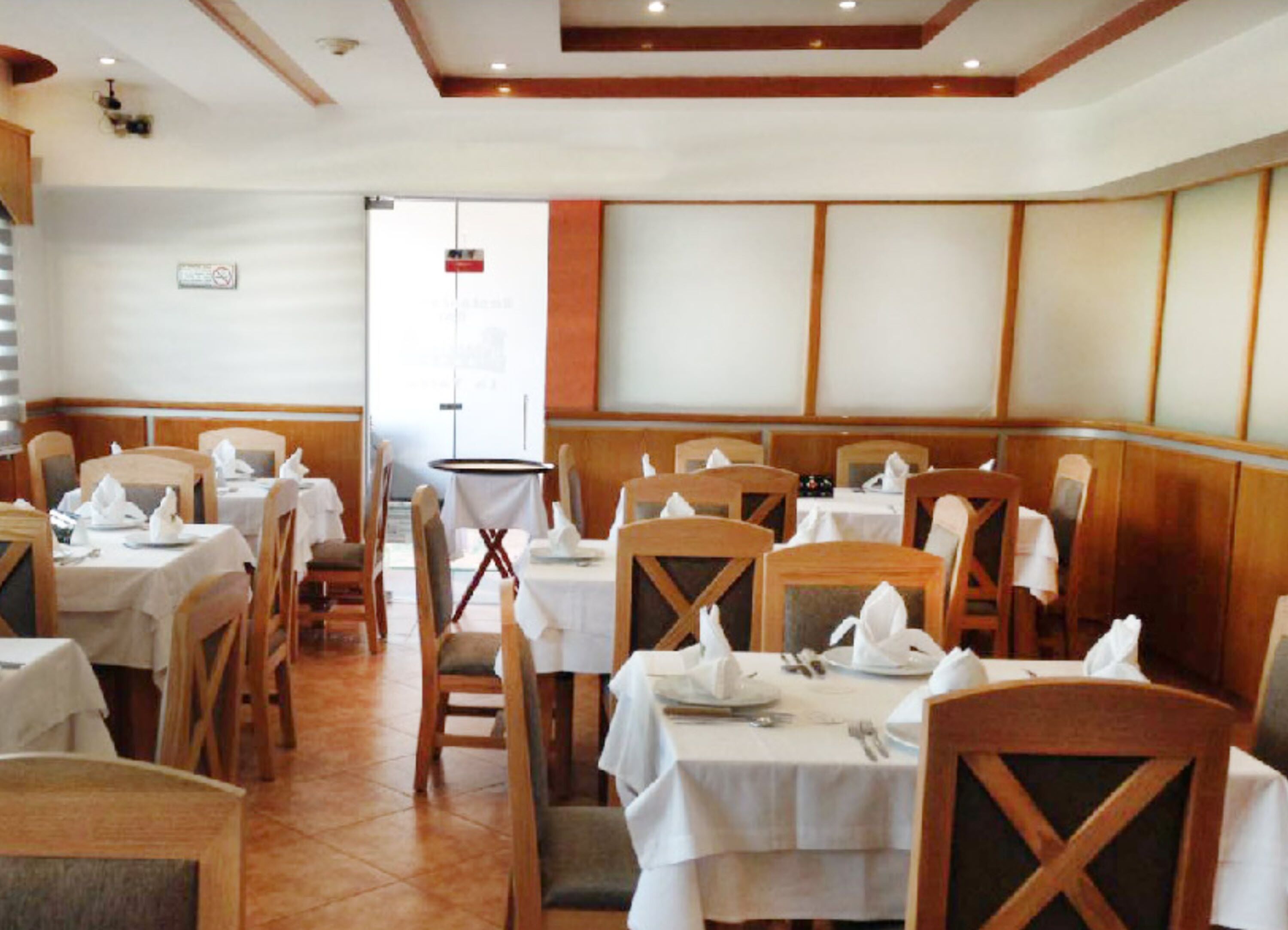 A restaurant with wooden chairs and tables, white tablecloths, and a tiled floor.