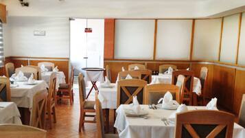A restaurant with wooden chairs and tables, white tablecloths, and a tiled floor.
