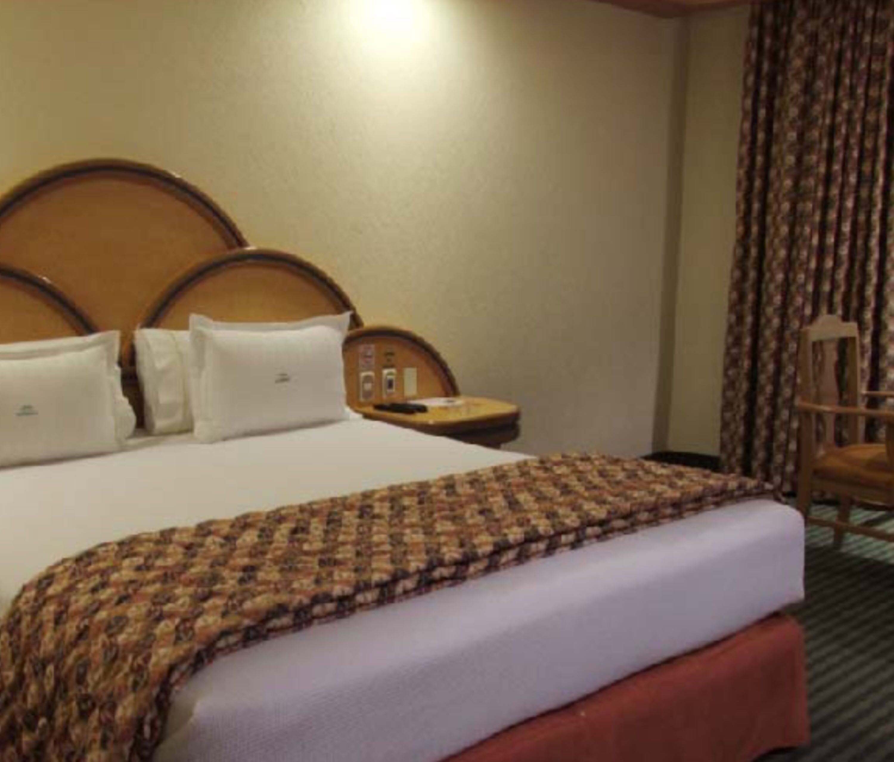 Ein Hotelzimmer mit einem großen Bett, einem Holz-Kopfteil, einem Nachttisch mit Lampe und einem Sessel.