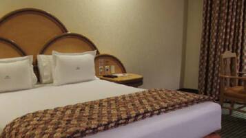 Ein Hotelzimmer mit einem großen Bett, einem Holz-Kopfteil, einem Nachttisch mit Lampe und einem Sessel.