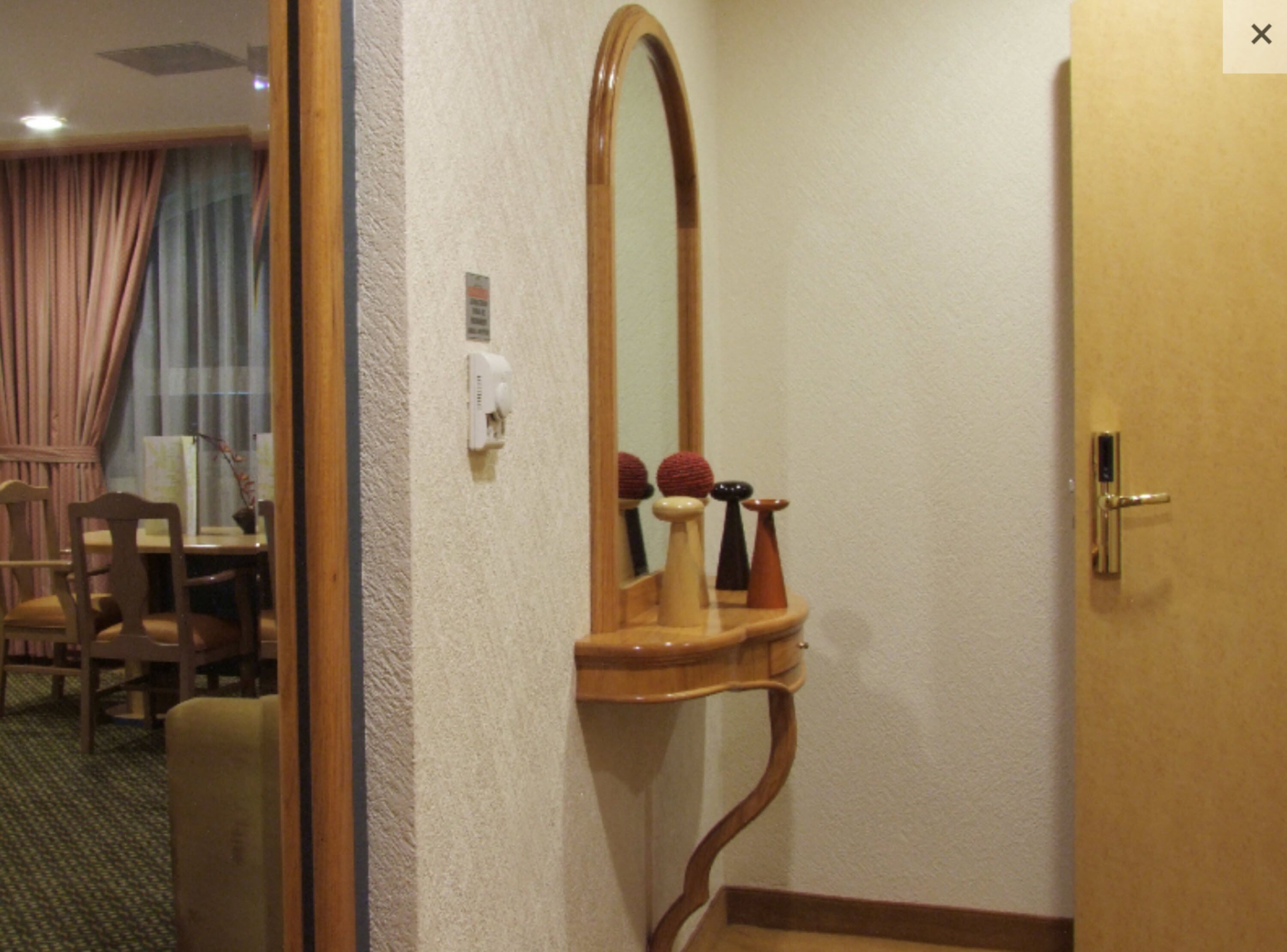 Une chambre d’hôtel avec une porte en bois, un miroir et une petite étagère en bois ornée d’objets décoratifs.