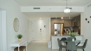 A modern kitchen with stainless steel appliances, a dining area with a glass table and chairs, and a hallway with a white door and a potted plant. - Luxury apartment in Doral miami, 1 Bd (Doral)