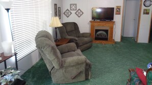 Una sala de estar con dos sillones reclinables, un televisor sobre un mueble bajo, una chimenea y una puerta.