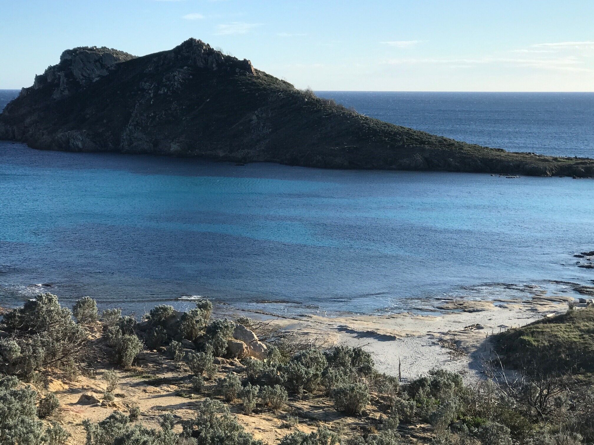 Un paisaje costero con una colina rocosa destacada y una playa de arena.