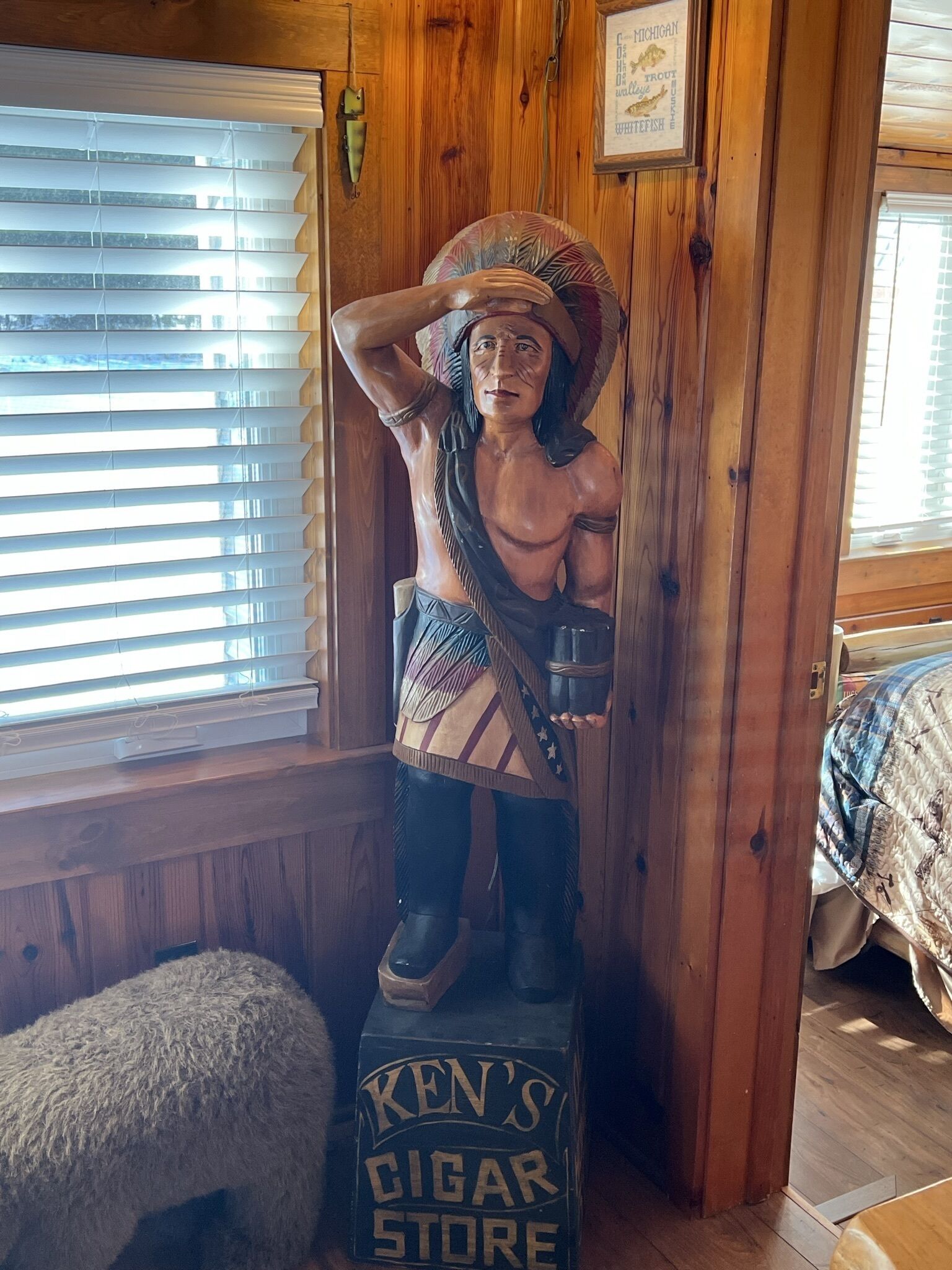 Et træinteriør med en statue af en indianerfigur, der holder en hat og en cigaræske med påskriften "KEN'S CIGAR STORE".