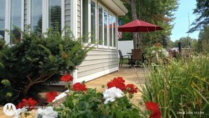 Una casa con un portico coperto, un ombrello rosso e un piccolo giardino con fiori rossi e bianchi.