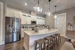 Une cuisine moderne avec des meubles blancs, des appareils en acier inoxydable et un îlot central doté de tabourets.