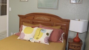 A bedroom with a wooden headboard, a bed with a yellow bedspread, and two pillows with a cartoon face design. There is a nightstand with a red lamp and a drawer. - Cozy Villa 10 minutes walk to riverwalk, Hemispher park and convenstion center. (San Antonio)