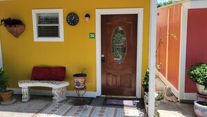 A yellow house with a wooden door, a bench, a potted plant, and a clock on the wall. - Cozy Villa 10 minutes walk to riverwalk, Hemispher park and convenstion center. (San Antonio)