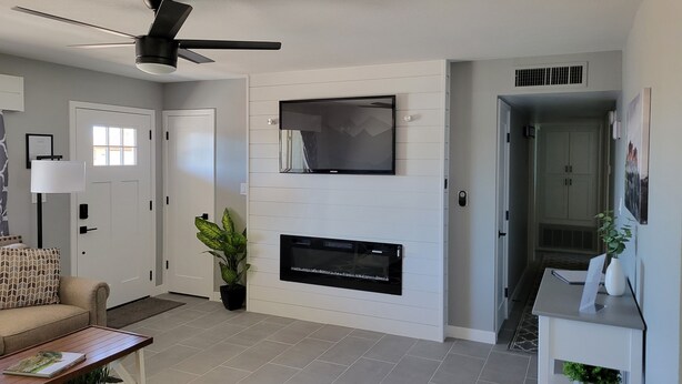 A modern living room with a flat-screen TV mounted on the wall, a ceiling fan, and a fireplace. - Lodging and entertainment all wrapped into one great place! (Apache Junction)