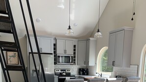A modern kitchen with white cabinets, a central island with bar stools, a wooden ladder, and a dining area with a sofa and coffee table. - Brand new chalet (cabin) on Beaver Lake in the Ozark Mountains!. (Garfield)