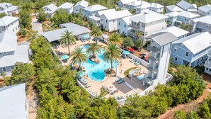 Ett hotellkomplex med flera byggnader, en central pool omgiven av palmer och utomhusområden med sittplatser.