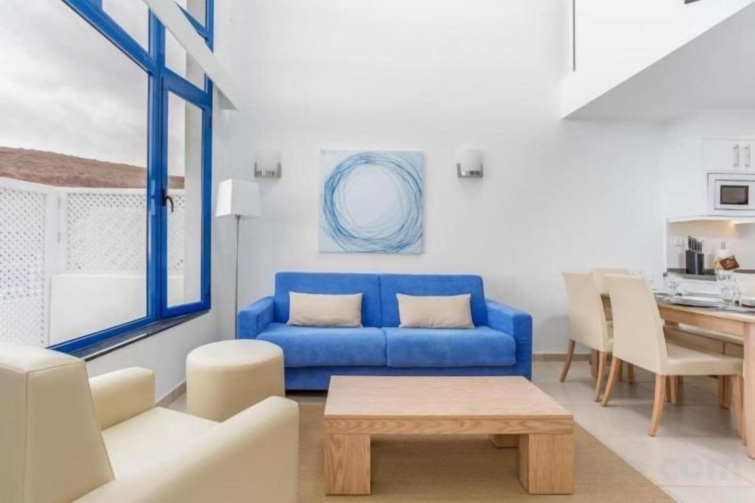 Una sala de estar moderna con un sofá azul, una mesa de centro de madera y una zona de comedor con sillas y una mesa.
