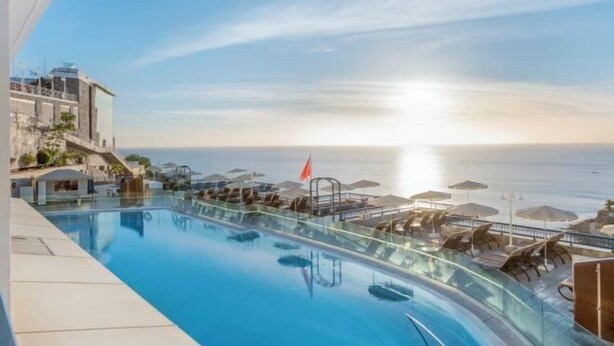 A poolside area with lounge chairs and umbrellas, overlooking a body of water. - Club Cala Blanca (MOGAN)