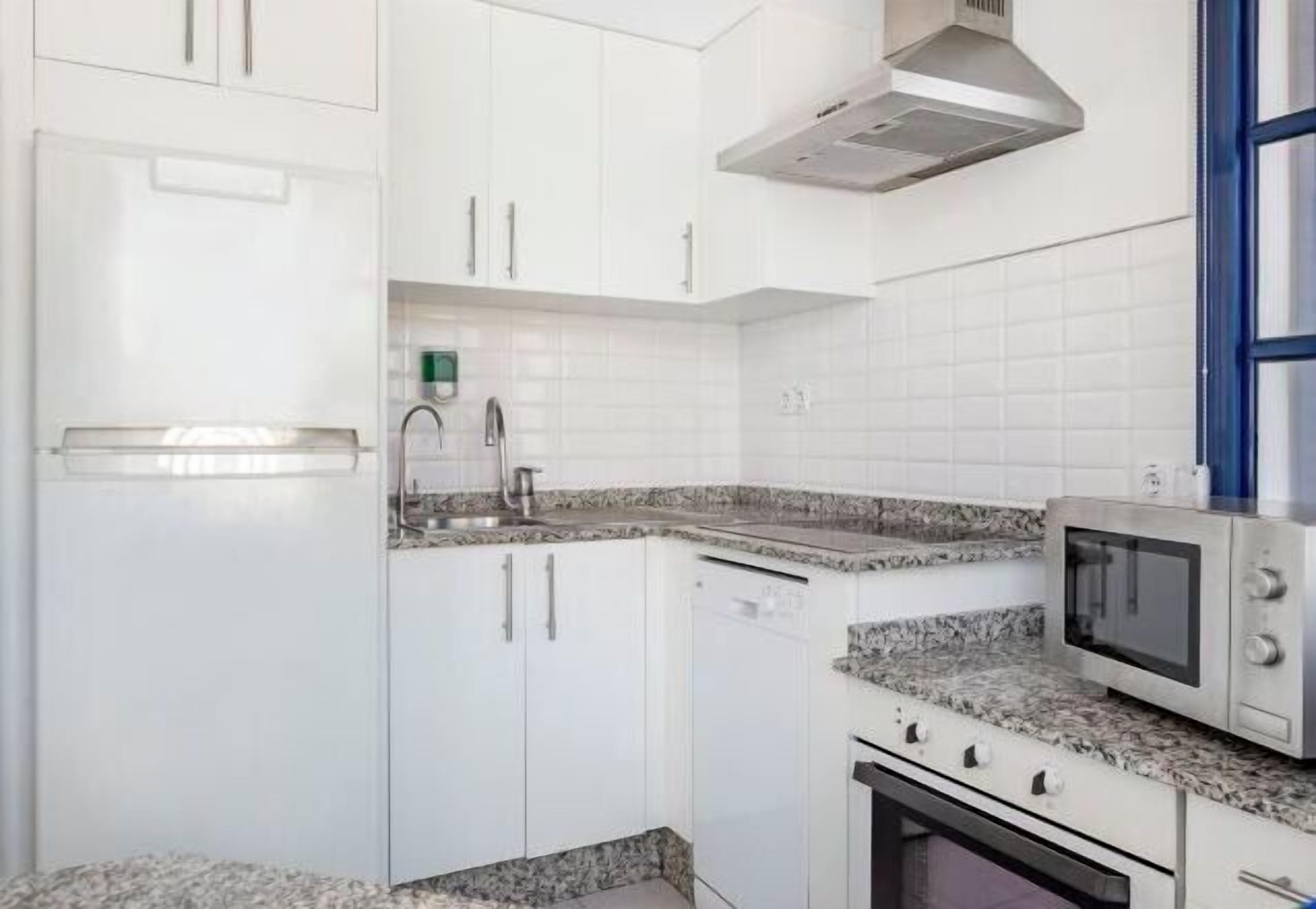 Una cocina con armarios blancos, encimera de granito, microondas y lavavajillas.