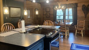 A rustic cabin interior with a central island stove, wooden dining table, and chairs. - log home Only 10 min from Mammoth Cave Nat Park (Park City)