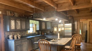 A spacious kitchen with dark wooden cabinets, a large island with bar stools, and hanging pendant lights. - log home Only 10 min from Mammoth Cave Nat Park (Park City)