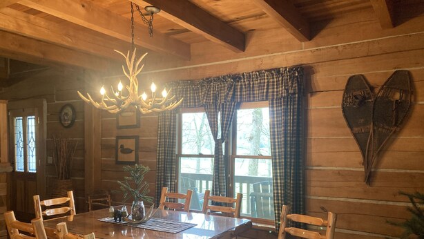 A rustic wooden dining room with a large table and chairs, a chandelier, and plaid curtains. - log home Only 10 min from Mammoth Cave Nat Park (Park City)