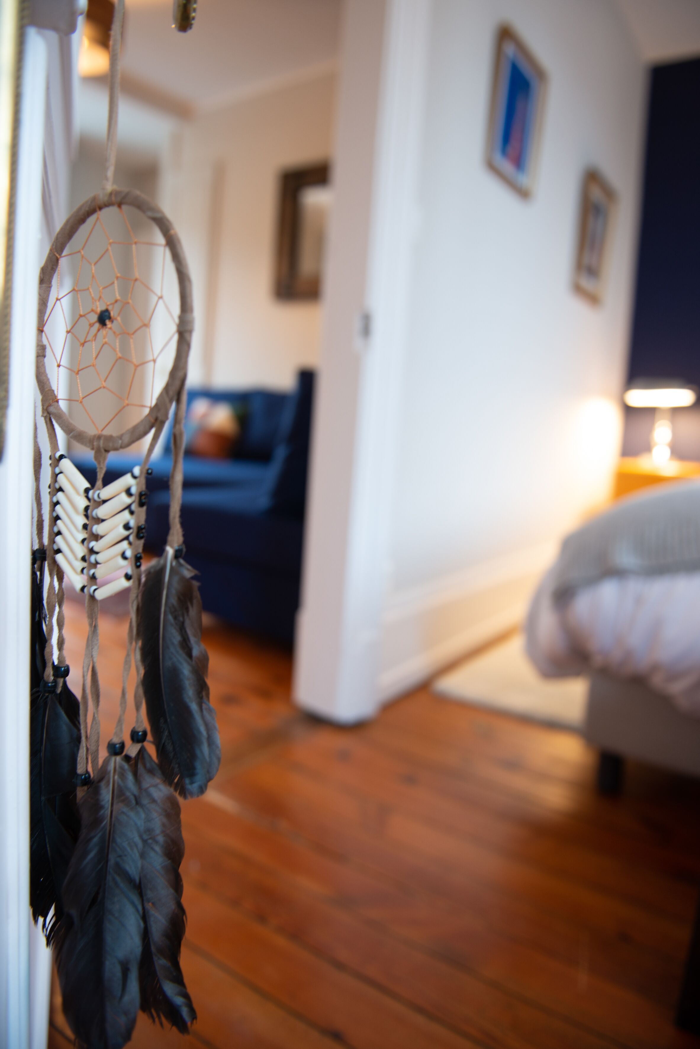 Ein Zimmer mit Holzboden, einem Bett, einem blauen Sofa und einem Traumfänger an der Wand.