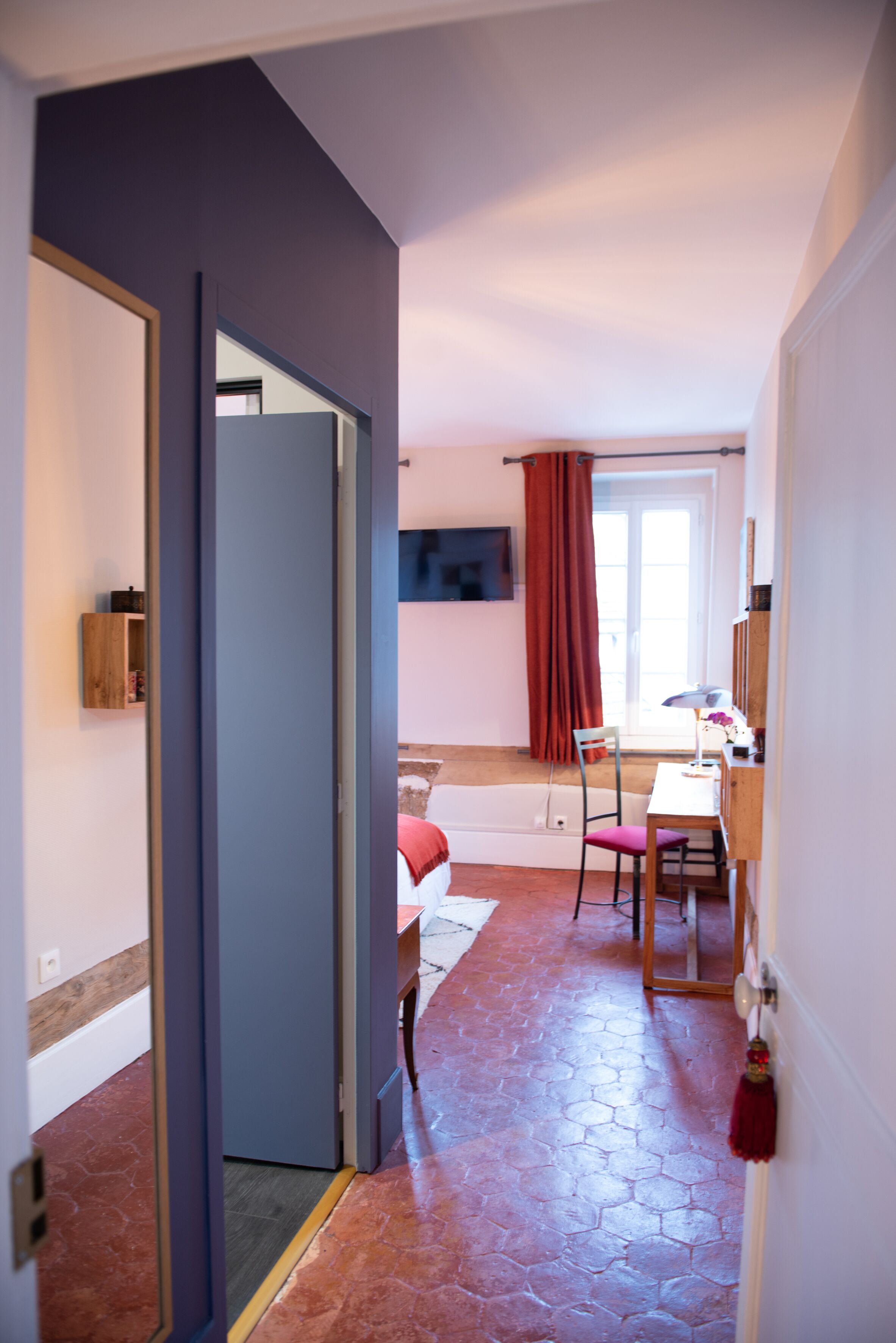 Ein Zimmer mit einem Bett, einem Schreibtisch, einem Stuhl, einem Fernseher und einem fensterbepflanzten Fenster.