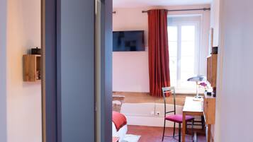 Ein Zimmer mit einem Bett, einem Schreibtisch, einem Stuhl, einem Fernseher und einem fensterbepflanzten Fenster.