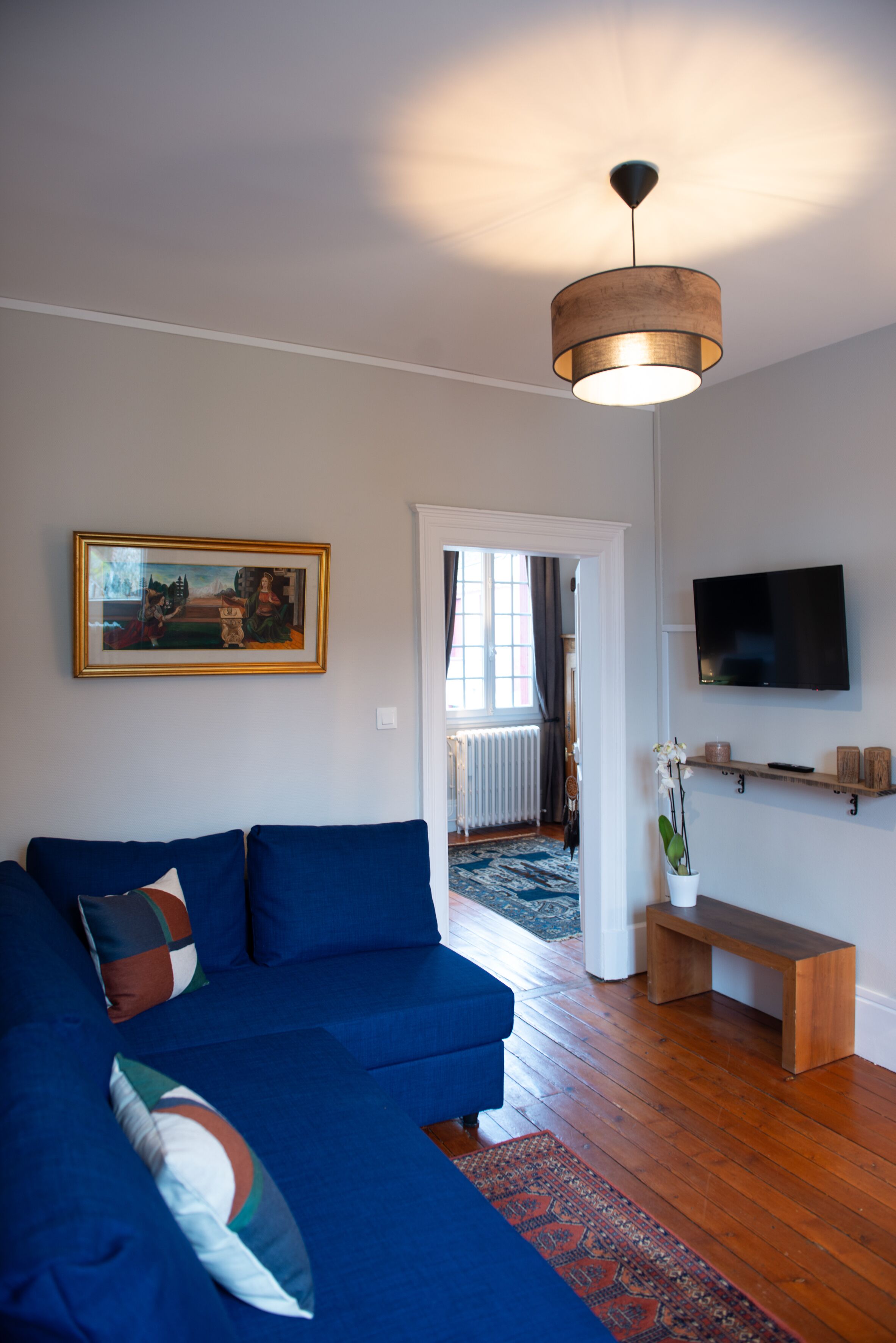 A living room with a blue sofa, a painting on the wall, a television, and a wooden bench.