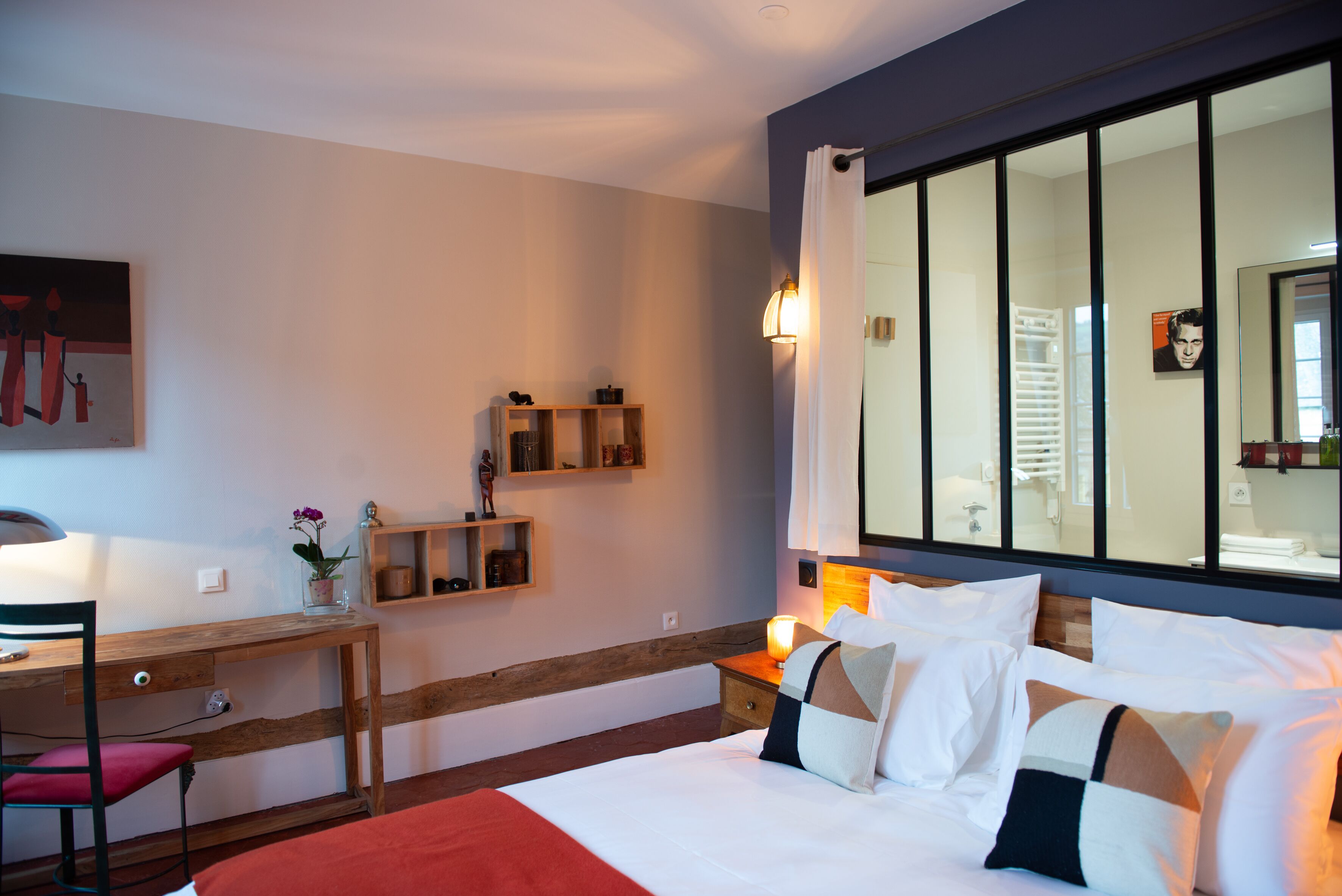 Een hotelkamer met een bed, een bureau, een stoel, een nachtkastje, een spiegel en een raam met gordijnen.