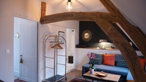 Una sala de estar acogedora con techo de madera, un sofá azul con cojines naranjas, una mesa de centro y una planta colgante.